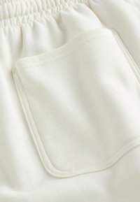 Primo piano di tessuto elastico bianco per fascia in vita con tasca rettangolare cucita su una superficie morbida e liscia.