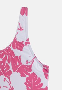 Maillot de bain avec un fond en tissu blanc orné de grands motifs floraux roses, des bretelles fines et ajustables, et des coutures sans couture.