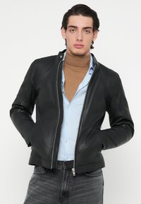 Zwarte leren jas met een ritssluiting aan de voorkant, slanke pasvorm, voorzien van een opstaande kraag en subtiele stikdetails op de schouders.