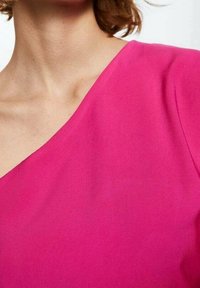 Top fuchsia avec un décolleté diagonal, en tissu lisse, doté d'une coupe ajustée et d'un léger éclat. Conçu pour une silhouette élancée.