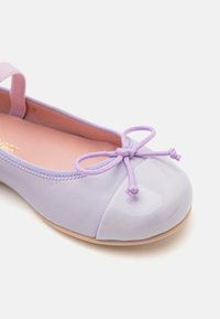 Baletă lilac cu vârf glossy, corp moale mat și detaliu sub formă de fundiță lilac. Dispune de o curea elastică pentru a se ajusta bine.