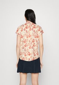 Blusa a maniche corte in un leggero colore pesca con un motivo floreale in tonalità rosse e viola; presenta un giogo posteriore e un orlo arrotondato.