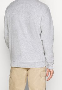 Grå, texturerad sweatshirt med långa ärmar och ribbade muddar, med rund halsringning och avslappnad passform, tillsammans med beige cargobyxor.