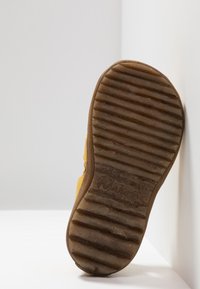 Žlutá gumová podrážka boty s texturovaným povrchem a vroubkovaným vzorem. Obsahuje logo a číslo "22" embosované na patě.