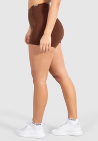 Bruine sportieve shorts met een hoge taille; soepele, rekbare stof; aansluitend ontwerp; gedragen met witte sportschoenen met zwarte accenten.