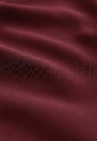 Bordová tkanina s hladkou textúrou, ktorá vykazuje jemný lesk a mäkké splývavé záhyby. Jednotná farba bez vzorov alebo kovových detailov.