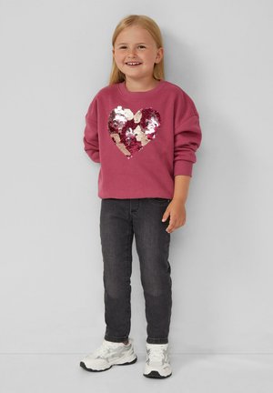 Fuksjowa bluza ze wzorem w kształcie serca z cekinami w kolorze różowym, srebrnym i złotym. Połączona z ciemnymi dżinsami i białymi sneakersami.