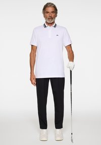 Biała koszulka polo z czarnym kołnierzykiem i akcentami, w połączeniu z czarnymi spodniami. Mężczyzna trzymający kij golfowy i noszący białe trampki.