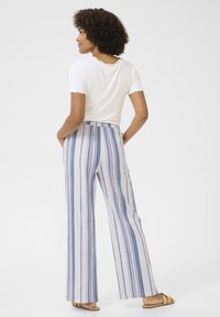 Witte geribbelde top met korte mouwen, gecombineerd met hooggewaisted wijdtaille gestreepte broek in blauw, roze en wit. Broek heeft zijzakken.