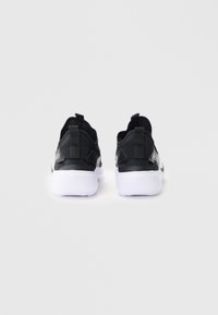 Baskets de sport noires avec une tige lisse, des accents texturés, des semelles blanches et des tirettes au niveau du talon pour un enfilage facile.