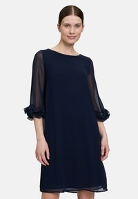 Robe droite bleu marine avec des manches longues transparentes. Accents froncés aux poignets et décolleté rond. Tissu lisse et léger.