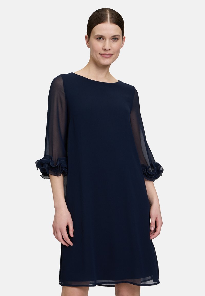 Robe droite bleu marine avec des manches longues transparentes. Accents froncés aux poignets et décolleté rond. Tissu lisse et léger.