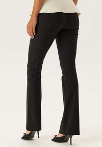 Zwarte denim flare jeans met een gladde textuur, details op de achterzak en een middelhoge tailleband. Gecombineerd met zwarte pointige hakken.