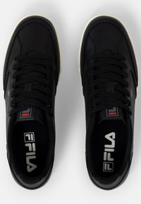 Svarta lädersneakers med platta snören, gummisulor och FILA-logotyp på tungan och innersulan. Har rena linjer och en minimalistisk design.