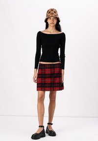 Must mustriba off-the-shoulder top, punane ja must karvane seelik, pruun ämbri müts lillemustriga ja jämedad mustad platvormisaapad.