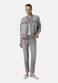 Grijze denimjas en bijpassende spijkerbroek, beide in een zachte textuur. Een zilveren platte schoen met een metallic afwerking maakt de outfit compleet.