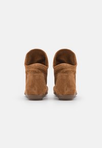 Beżowe zamszowe botki za kostkę o miękkiej fakturze, zaokrąglonym nosku, niskim obcasie i odkrytym wykończeniu, prezentujące prosty, nieozdobiony design.