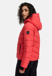 Red padded jacket with a hood, featuring horizontal quilted sections, a zip pocket, and a circular logo on the left sleeve.