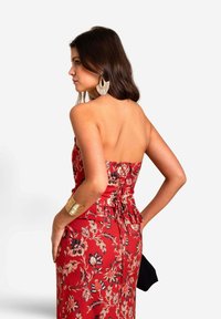 Rood bloemenprint jurk met een aansluitende lijfje, strapless ontwerp en een geplooide peplum taille. Onderscheidt zich door gouden accessoires en gekruld haar.