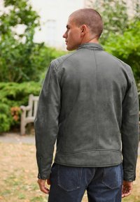 Giacca da uomo in pelle grigia con colletto alto, polsini con zip e dettagli a coste. Texture morbida, design minimalista e vestibilità su misura.