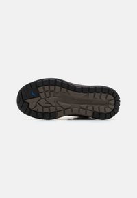 Suela de zapato de goma negra y marrón con un patrón de textura; presenta el nombre de la marca grabado y detalles en azul.