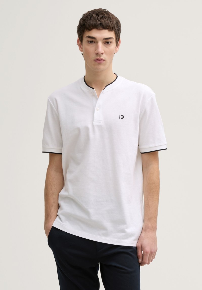 Tricou polo alb din bumbac, cu mâneci scurte, cu detalii negre la guler și la mâneci, având un mic logo pe partea stângă a pieptului.