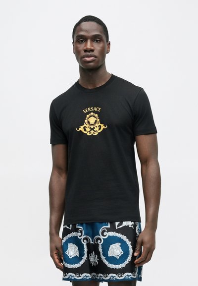 Tricou negru din bumbac, cu logo-ul "Versace" auriu și un design ornamentat pe piept. Mâneci scurte și guler rotund.