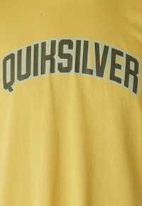Yellow T-shirt with a soft texture features "QUIKSILVER" in bold green letters outlined in light blue across the chest.