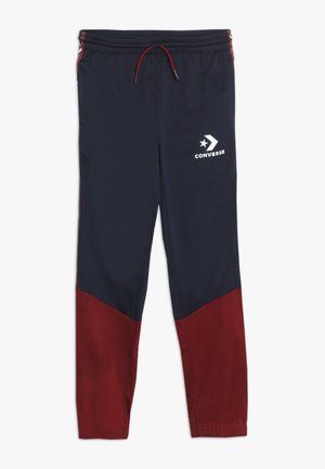 Pantalon de survêtement Converse bleu marine et rouge foncé avec taille élastique, cordon rouge et logo blanc Converse sur la partie supérieure de la cuisse gauche.