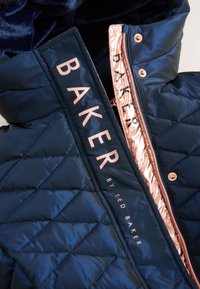 Marineblauw doorgestikt jack met een glanzende afwerking, voorzien van roségouden hardware, een contrasterende voering en opvallende tekstbranding op de kraag.