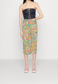 Top sans bretelles en denim avec un détail de laçage à l'avant, associé à une jupe enveloppante colorée à motifs floraux et des chaussures à plateforme roses avec un motif à carreaux.