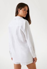 Hvid linnedskjorte med lange ærmer, krave og knappede manchetter. Har en rygskuldre design og en afslappet pasform.