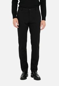 Schwarze Hosen mit schlanker Passform, aus glattem Stoff, mit Knopfverschluss und seitlichen Taschen. Getragen mit schwarzen, glänzenden Schuhen.