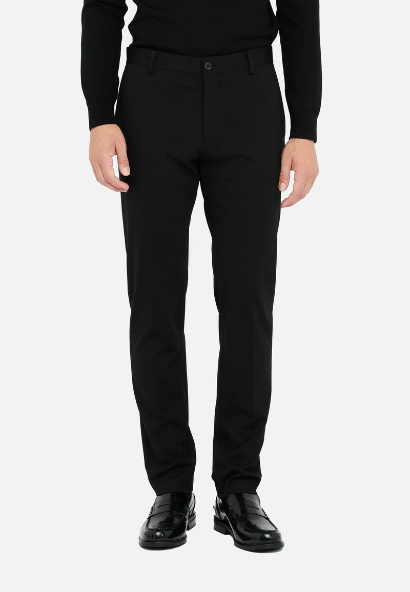 Schwarze Hosen mit schlanker Passform, aus glattem Stoff, mit Knopfverschluss und seitlichen Taschen. Getragen mit schwarzen, glänzenden Schuhen.