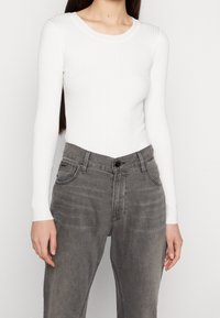 Bílý žebrovaný top s dlouhým rukávem v kombinaci se šedými džíny, který se vyznačuje přiléhavým střihem a klasickým kulatým výstřihem.