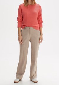 Koronowy sweter ribbed z długimi rękawami, zestawiony z beżowymi spodniami o szerokich nogawkach z guzikami i fałdami z przodu, stylizowany z białymi trampkami.