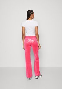 Rosa velourbyxor med utsvängd form och en silvrig rhinestones-logotyp på baksidan. Kombineras med en figurnära vit t-shirt med kort ärm.
