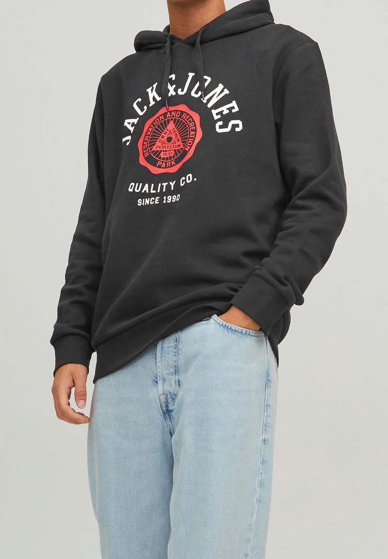 Schwarzer Kapuzenpullover mit weißen und roten Drucklogos. Weicher Stoff, lange Ärmel, elastische Bündchen, mit einer Fronttasche, kombiniert mit hellblauen Jeans.