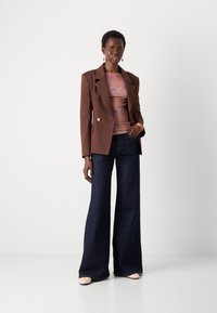 Brun dobbeltradet blazer, rosa grafisk topp, mørkeblå vide jeans, kremfargede sko, gulløredobber, glatte teksturer, avslappet passform.