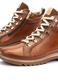 Brown leather ankle boots with a smooth finish, cream laces, a side zipper, gold-tone hardware, and a textured brown rubber sole.