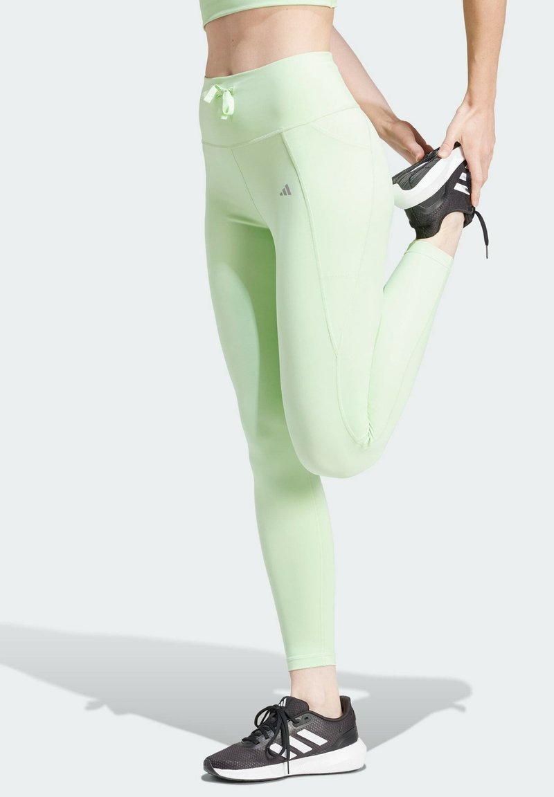 Persona che indossa leggings verde chiaro e sneaker neri Adidas si allunga i quadricipiti tirando un piede verso i glutei.