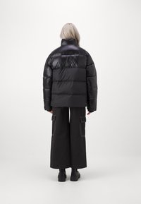Schwarze Puffy-Jacke mit hohem Kragen, gestepptem Design und weiter Silhouette. Kombiniert mit locker sitzenden, dunklen Cargo-Hosen und klobigen schwarzen Stiefeln.