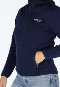 Giacca zip-up navy realizzata in tessuto testurizzato, con colletto alto, tasche laterali e un logo sul petto.
