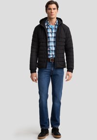 Schwarze Steppjacke mit Kapuze, darunter ein blaues kariertes Hemd, blaue Jeans und schwarze Sneaker mit Gummisohlen. Einfaches, praktisches Design mit Reißverschlüssen.