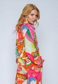 Farbenfrohes, lockeres Kleidungsstück mit einem lebhaften floralen und geometrischen Muster in Pink, Grün, Orange und Blau. Aus leichtem Stoff.