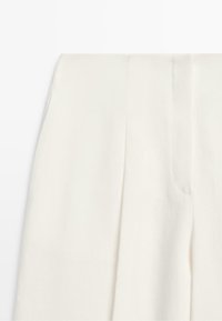 High-waist white trousers with a front pleat and concealed fastening shown from the waist to mid-thigh.