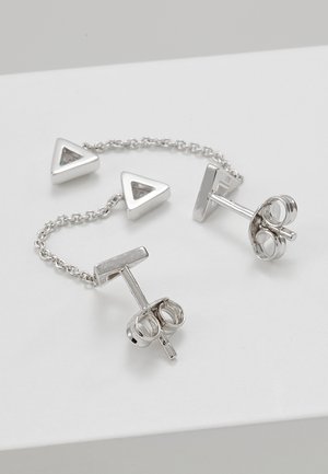 Boucles d'oreilles clous en argent reliées par une chaîne délicate, avec des formes triangulaires creuses ornées de petites pierres incrustées sur une surface blanche.