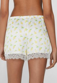Witte shorts met een citroenpatroon en groene bladeren. Decoratieve kantafwerking aan de onderkant voegt een textuurdetailelement toe. Elastische tailleband.