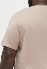 T-shirt kratkih rukava u svijetlo bež boji, izrađen od glatkog materijala. Ima okrugli izrez i čist, minimalistički dizajn.