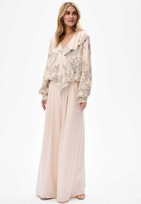 Beige blouse met bloemenpatroon en gerimpelde kraag, gecombineerd met lichte, wijdvallende broeken. Zachte, vloeiende stof met een losse pasvorm.